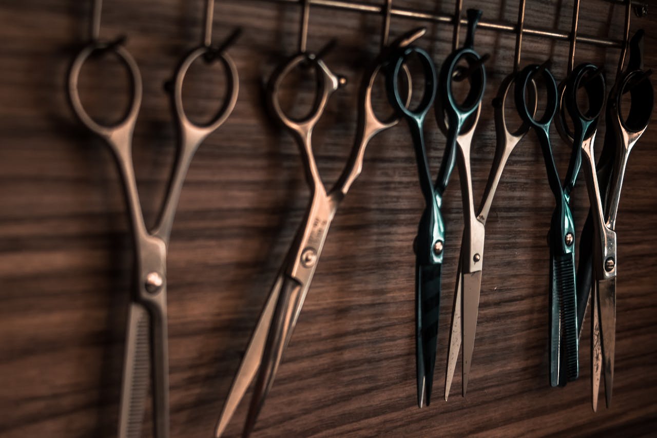 hero-img-02 A collection of vintage barber scissors hanging on a wooden wall, showcasing sharp tools for hair cutting.